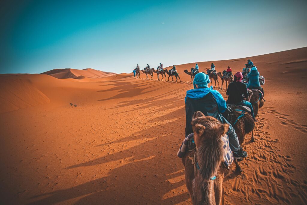 group of people riding camels through the Sahara desert in Merzouga